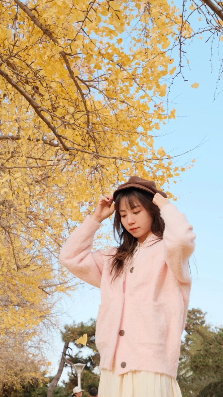 Woman in a pink cardigan under golden ginkgo trees, portrait