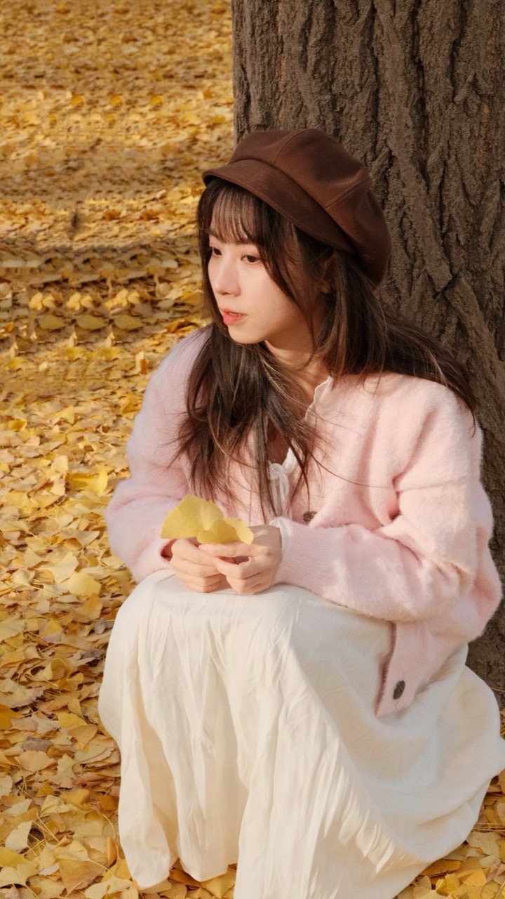 Woman sitting under a ginkgo tree holding a yellow leaf, portrait